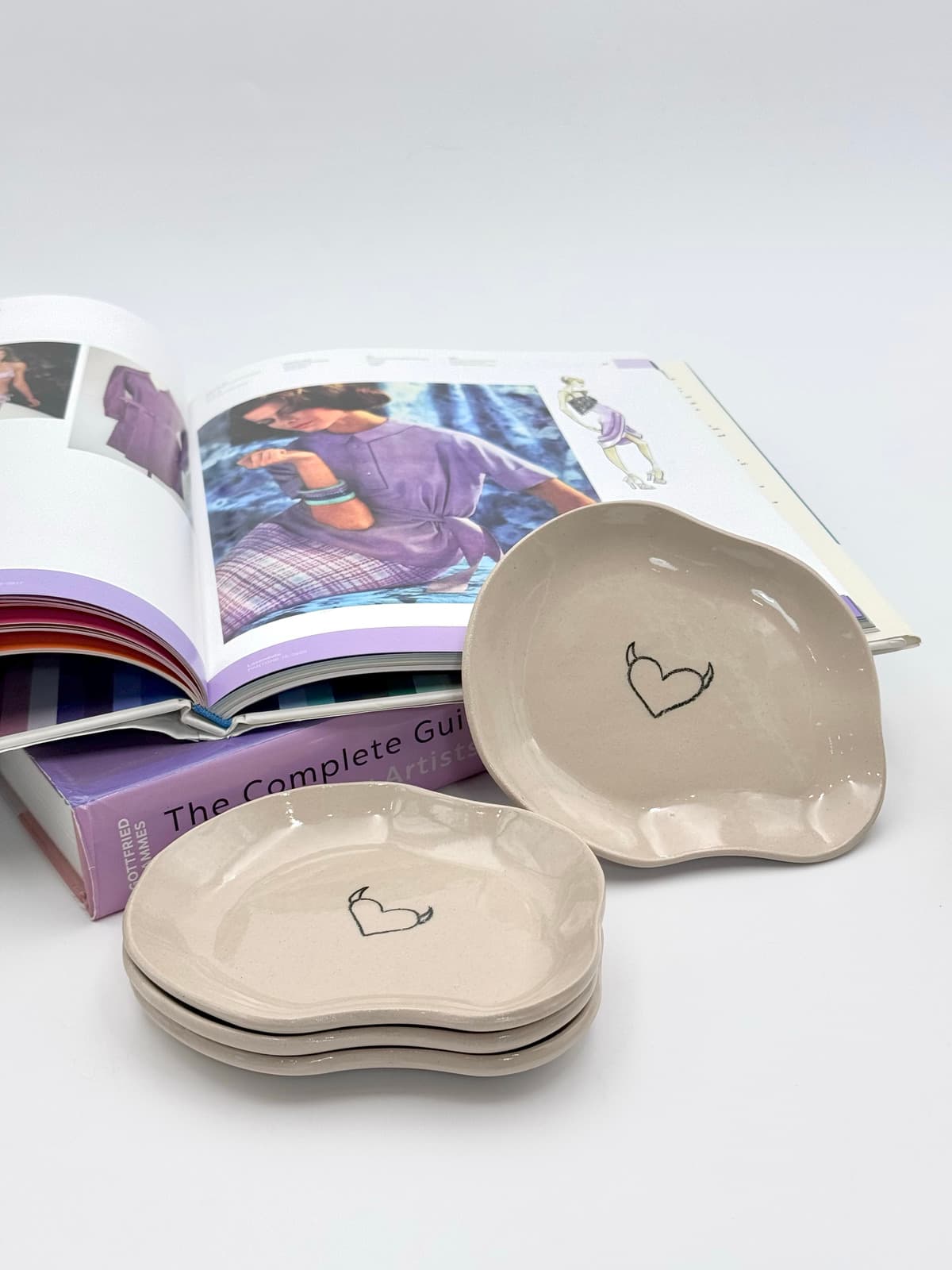 Handmade glossy beige ceramic trays with irregular organic shapes and black horned heart motif, shown stacked.
